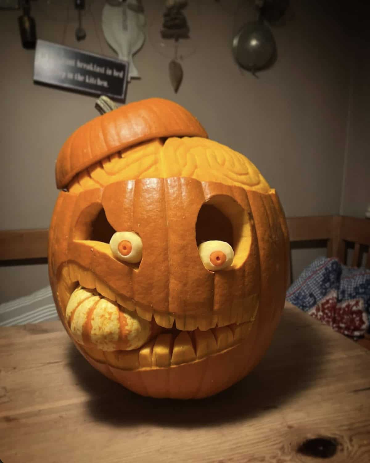 carved pumpkin with an exposed brain under a tilted lid, peeled potato eyeballs and a toothy grin biting a small gourd