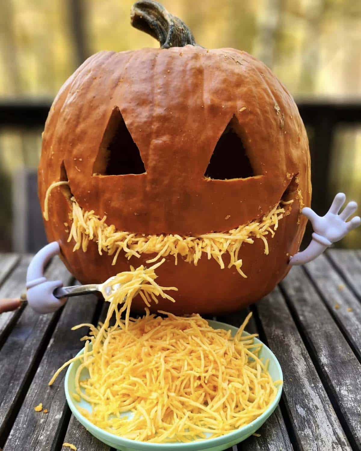 jack-o'-lantern with shredded pumpkin stuffed in its grinning mouth, cartoon glove hands holding a fork and a plate of shredded pumpkin in front