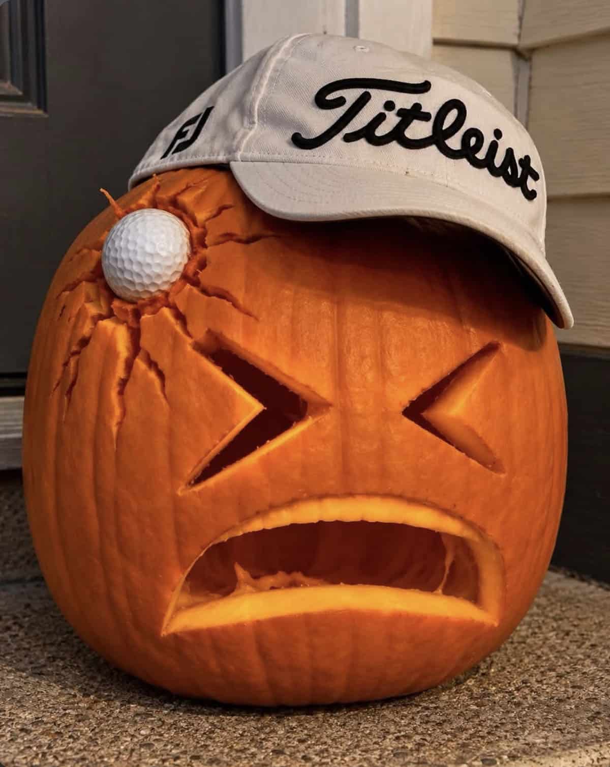 carved pumpkin with X-shaped eyes and a frown, a golf ball lodged in cracked skin and a golf cap on top