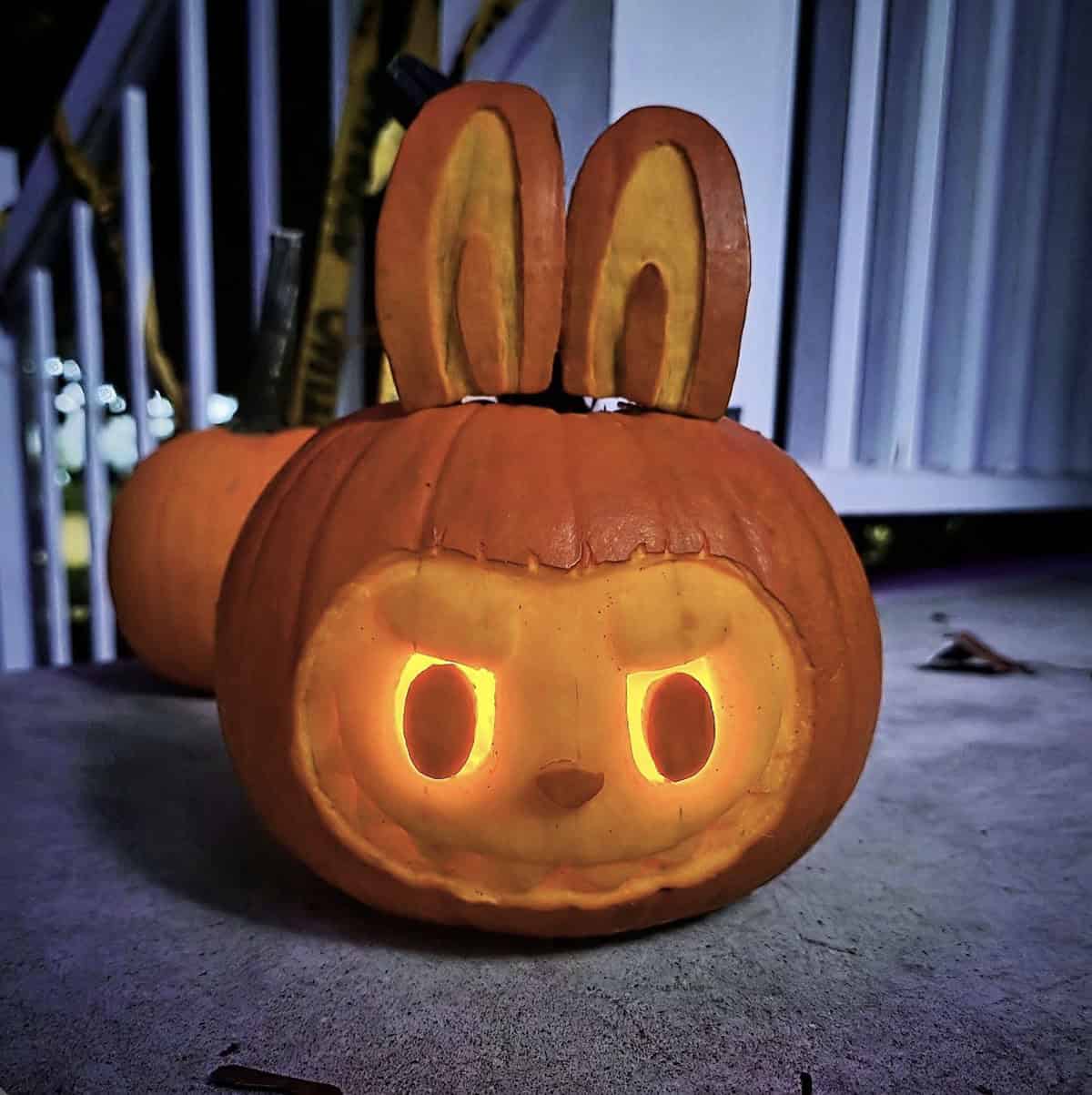 pumpkin carved like Labubu with bunny ears, a shaved face, glowing oval eyes and a toothy grin