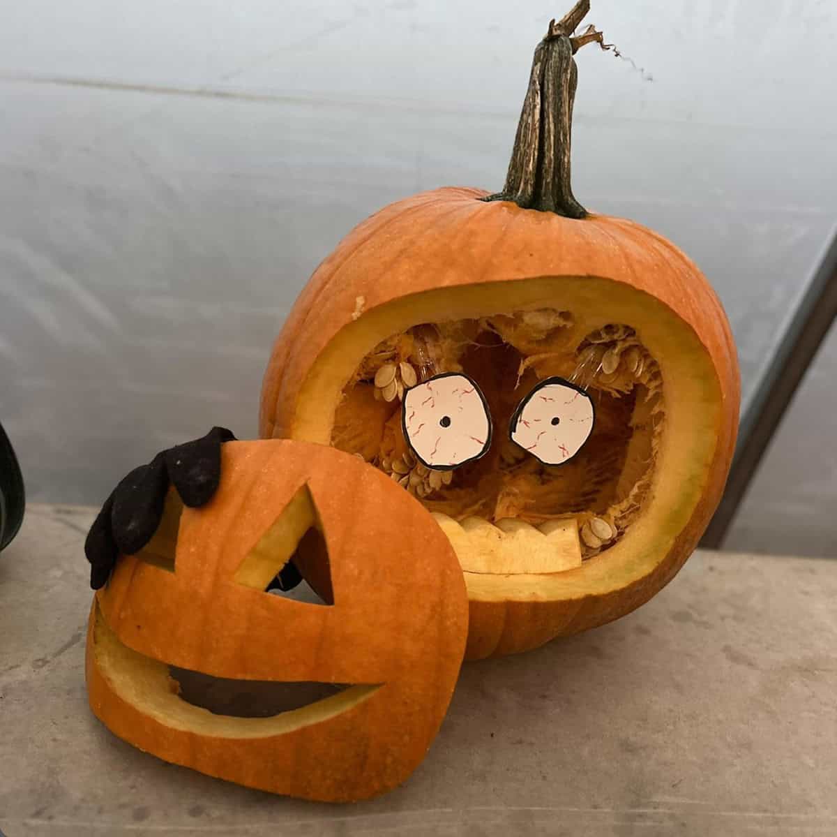 carved jack-o'-lantern face removed and propped in front of a hollow pumpkin, with shocked bloodshot paper eyes peering out from inside