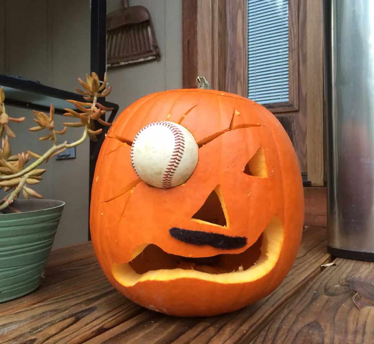 jack-o'-lantern with a black pipe cleaner mustache, a crooked grin and a baseball lodged in cracks around one eye