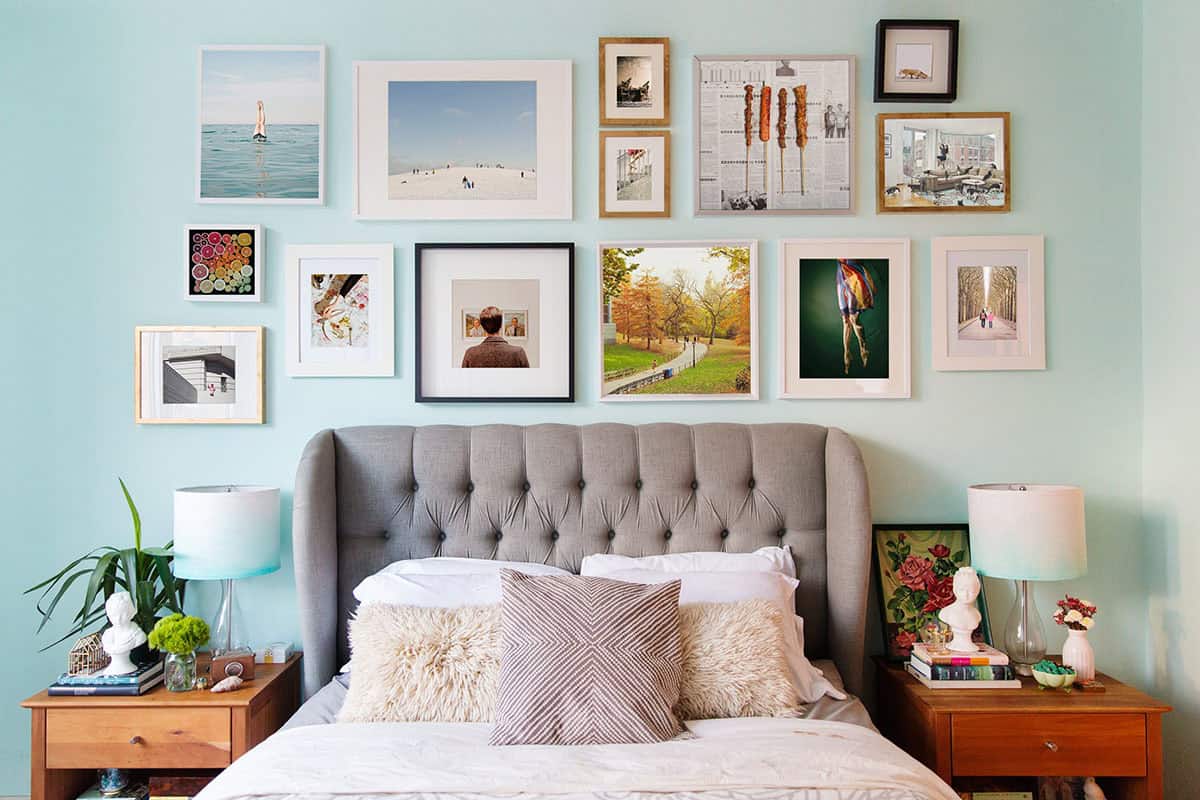 Bedroom gallery wall of framed photographs above a gray tufted headboard on an aqua wall
