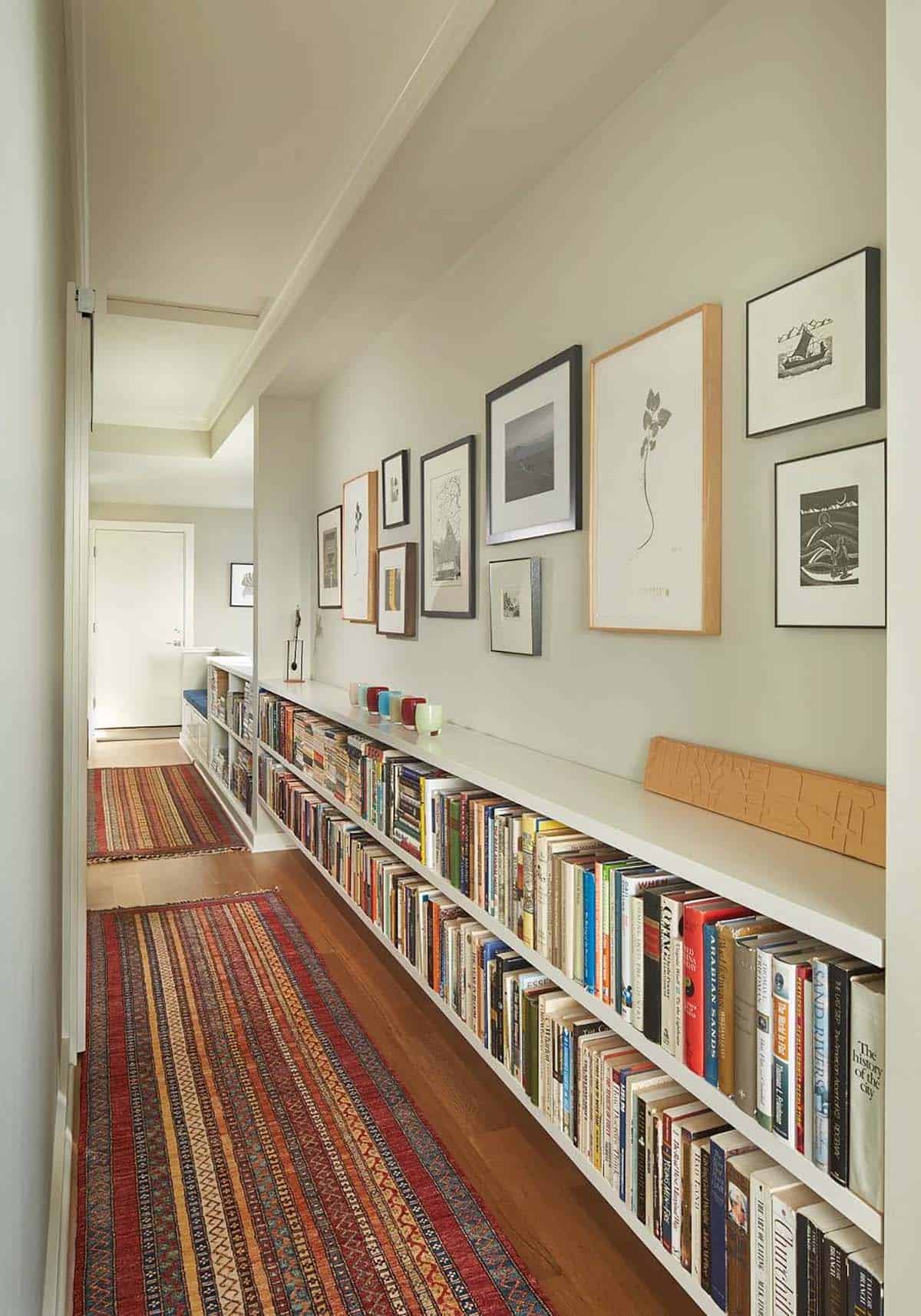 Long hallway with a gallery wall of framed prints above a low built-in bookshelf and striped runners