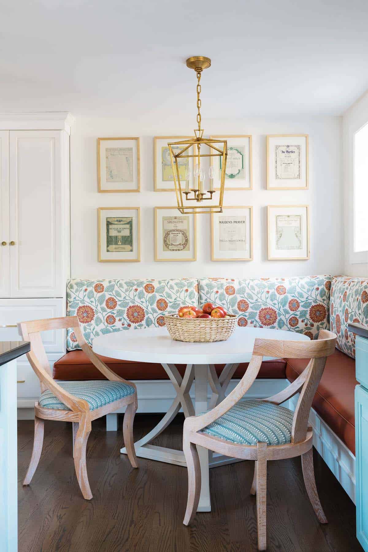 Breakfast nook with a symmetrical gallery wall of framed vintage sheet music above a floral banquette