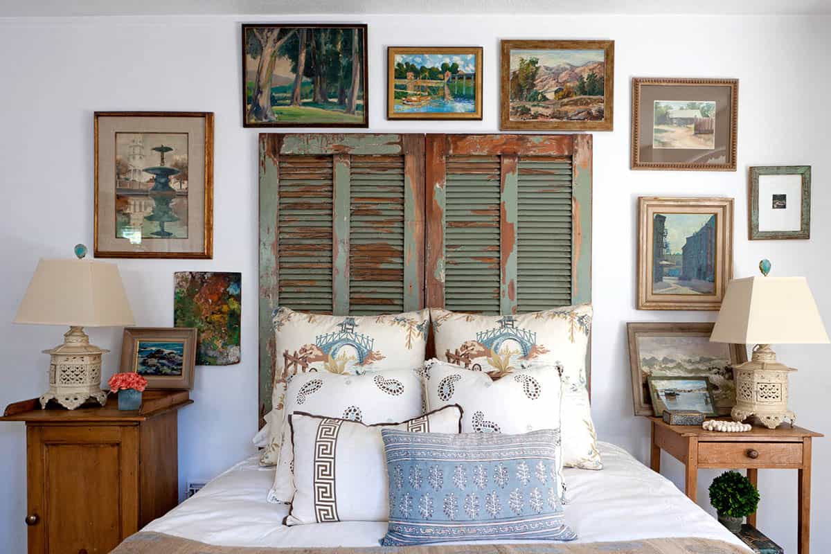 Bedroom gallery wall of vintage landscape paintings around a headboard made from old green shutters