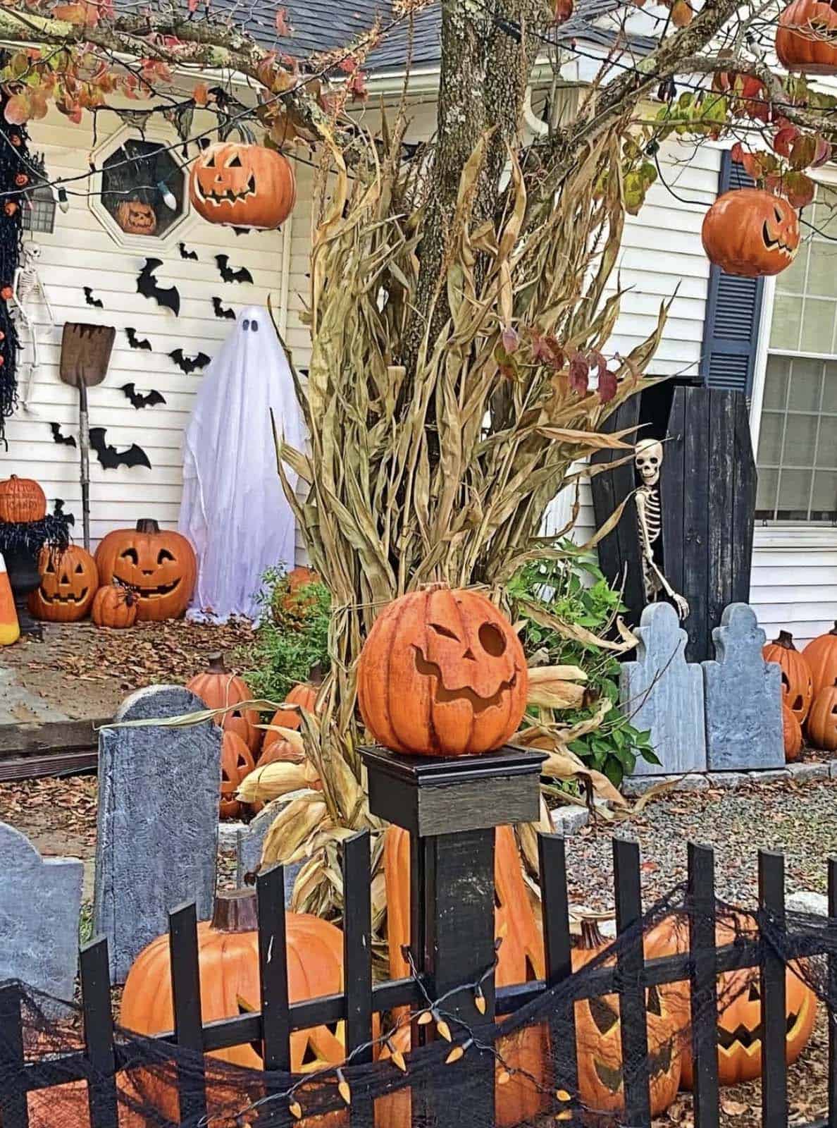 Black picket fence draped in cheesecloth with jack-o'-lanterns, cornstalks, foam tombstones, a ghost, and a skeleton peeking from a coffin