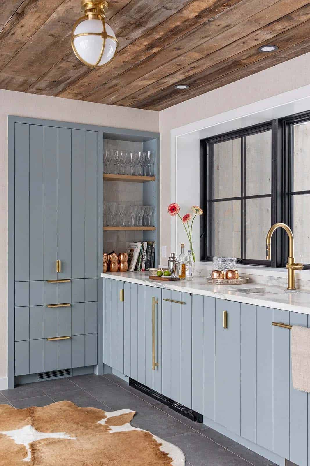 Powder-blue bar cabinetry with brass pulls, open glass shelving and a reclaimed wood plank ceiling