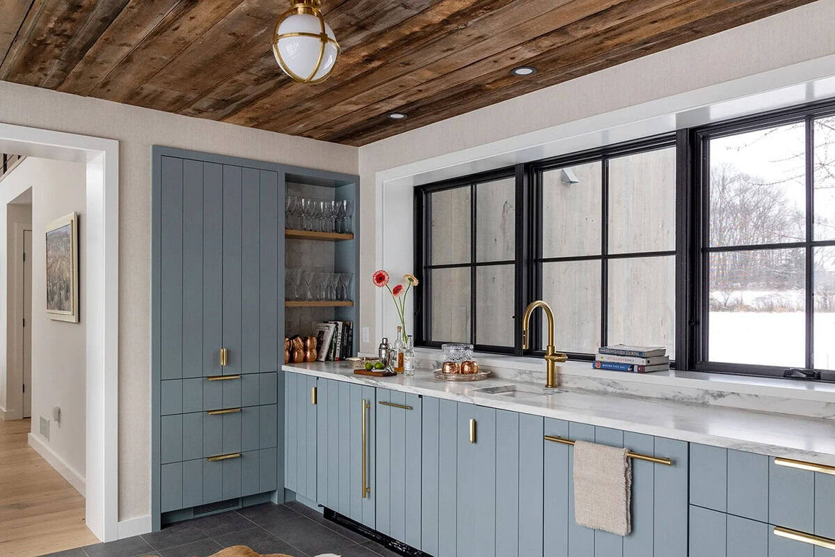 Wet bar with vertical-groove blue cabinets, marble counter and black-framed windows overlooking a snowy field