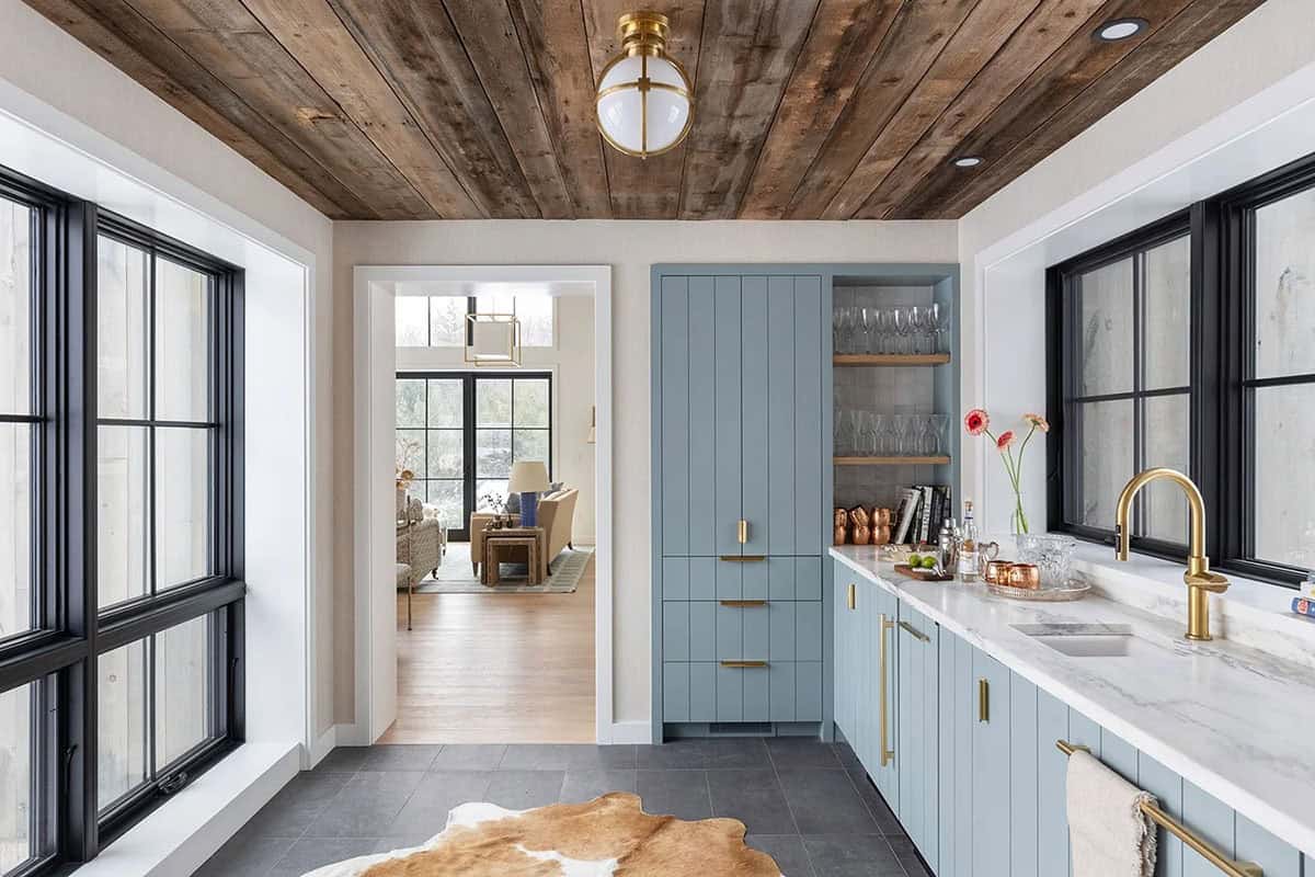 Narrow bar room with blue cabinetry and a cowhide rug, opening to a bright living room beyond