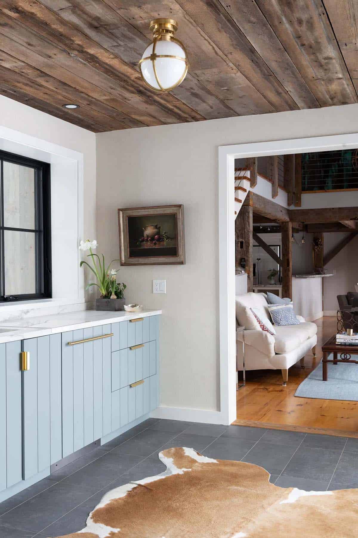 Blue bar cabinets and brass globe light beside a doorway to the timber-framed barn interior