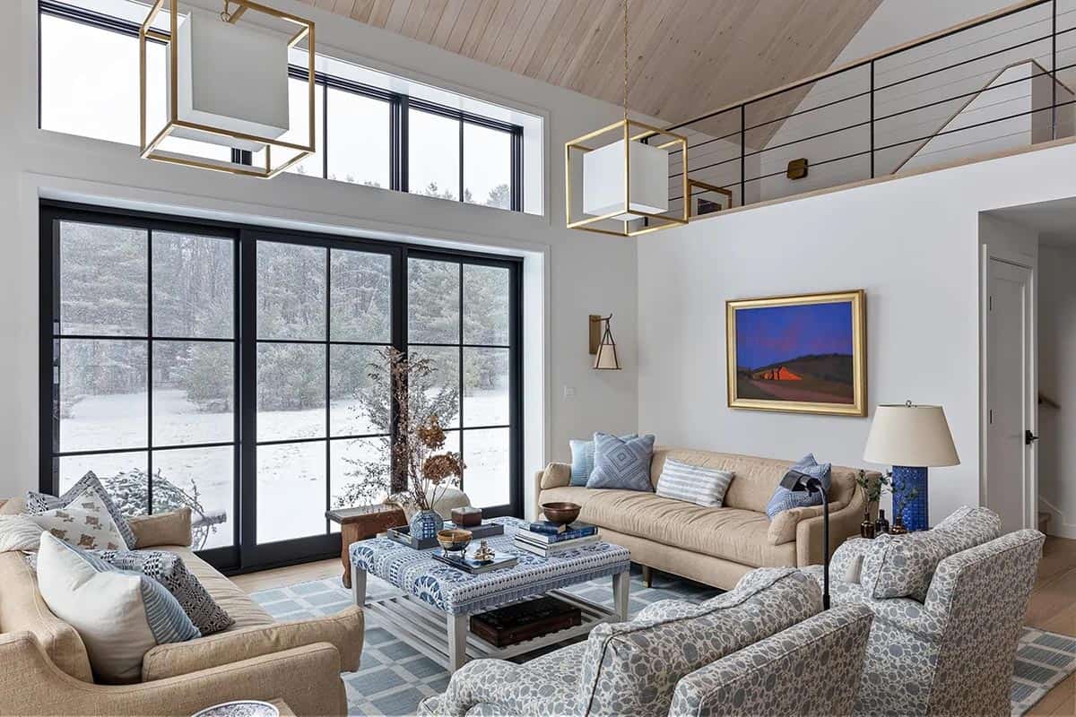 Living room with tall black-framed windows facing a snowy landscape and a red barn painting