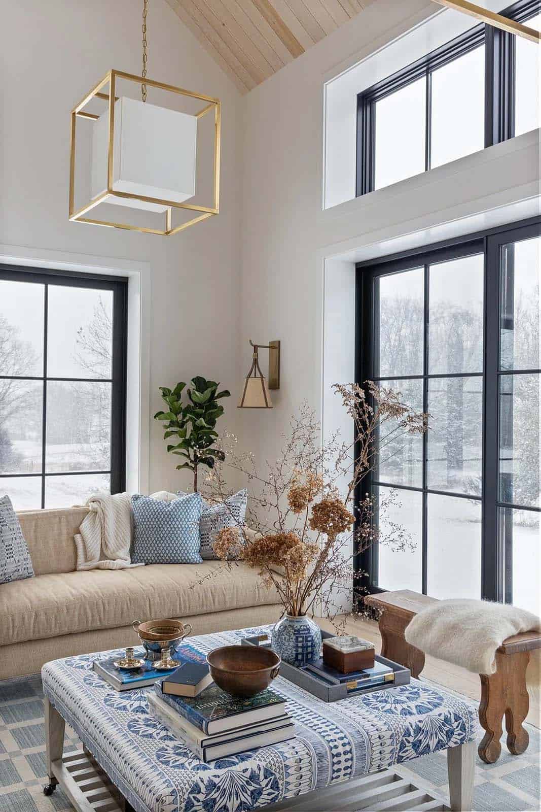 Close-up of a blue-and-white upholstered ottoman, dried hydrangeas and tall snowy windows