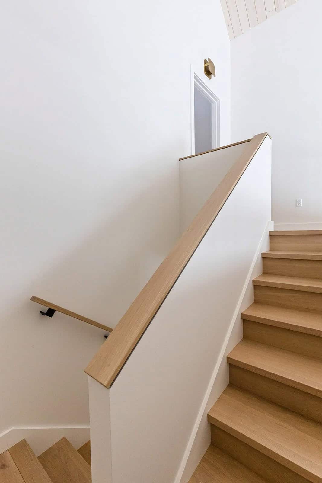 White oak staircase with a wide wood handrail and minimalist white walls