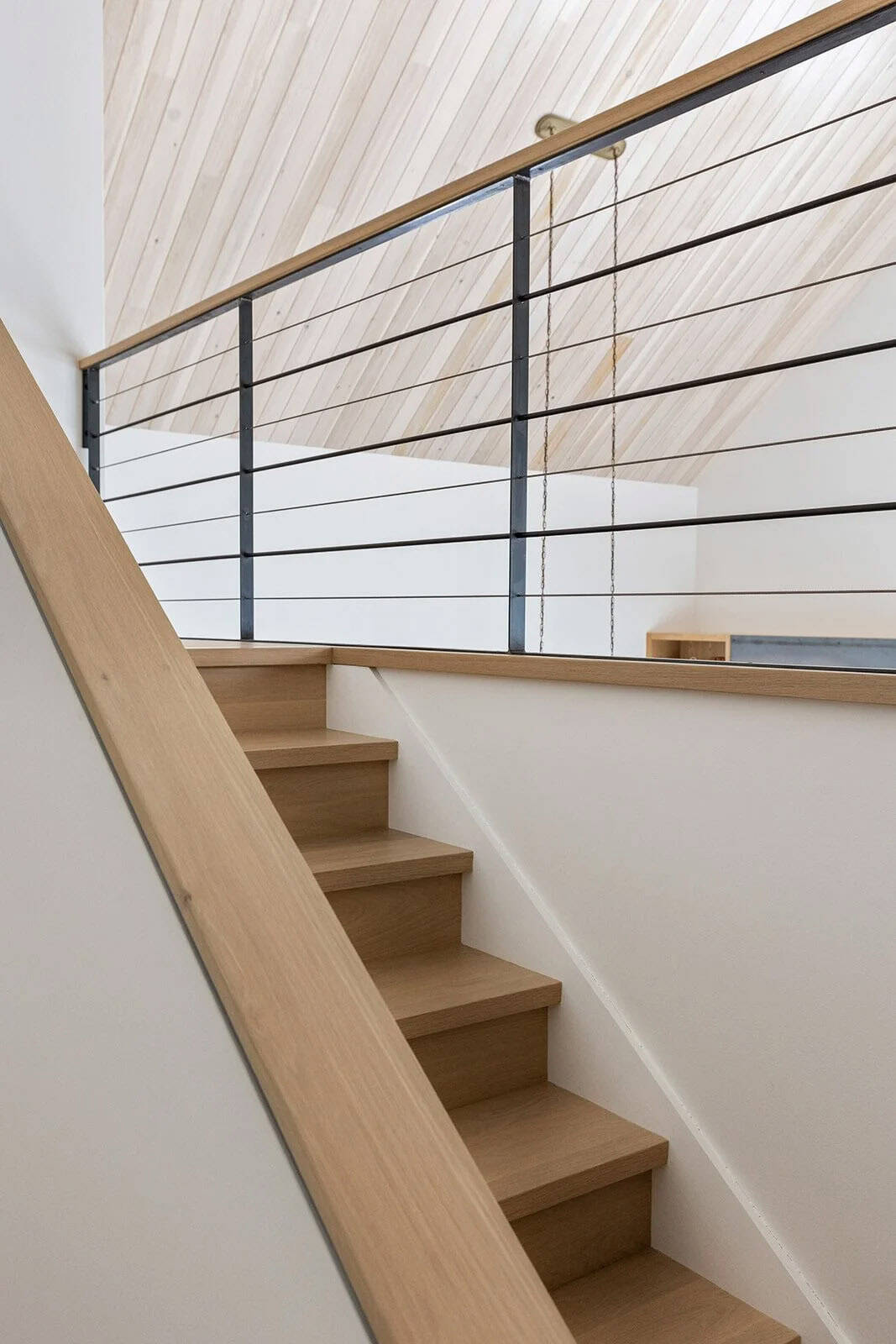 Oak stairs and loft landing with a black steel cable railing beneath a vaulted wood ceiling