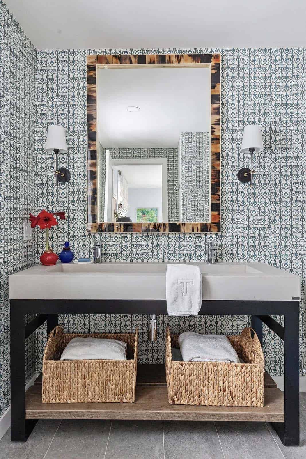 Bathroom with patterned blue wallpaper, horn-framed mirror and open concrete-top vanity