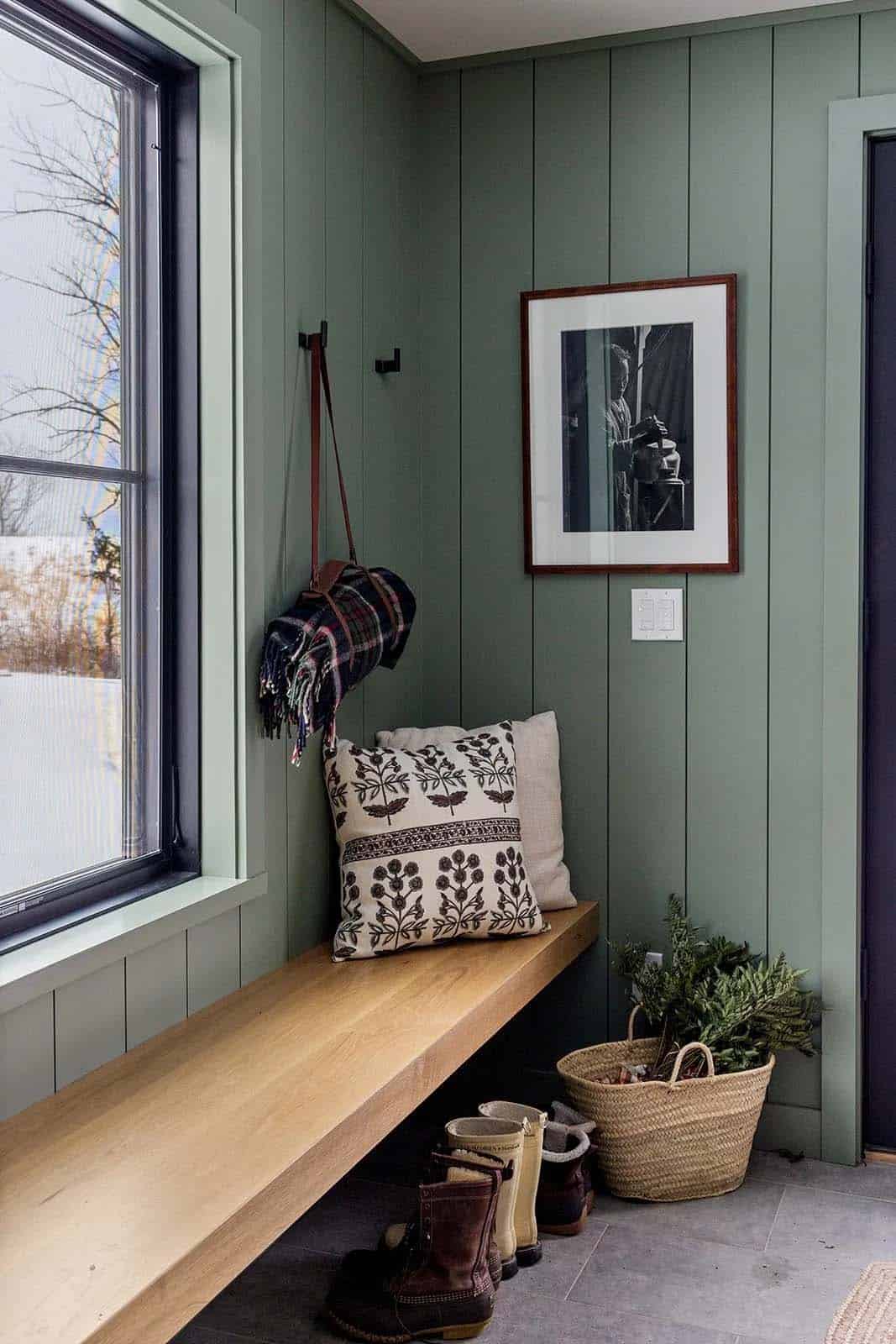 Mudroom with sage green paneling, a floating oak bench, winter boots and a plaid blanket