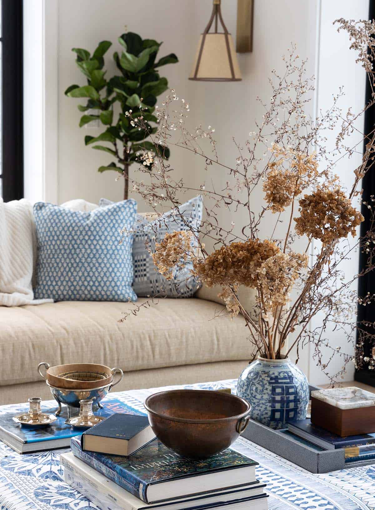 Close-up of dried hydrangeas in a blue-and-white vase on a patterned ottoman with stacked books