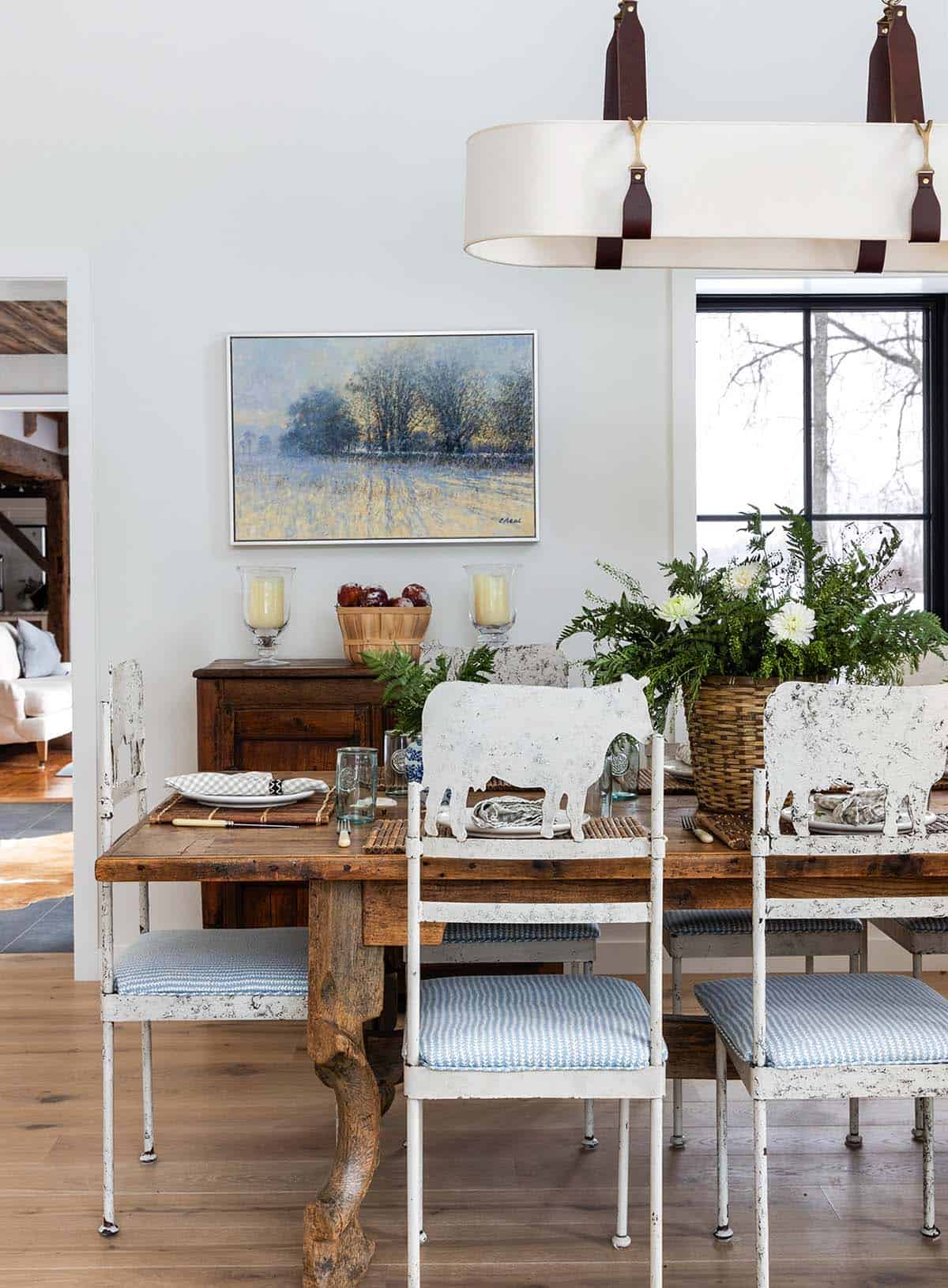 Rustic dining table with cow-shaped metal chairs and a landscape painting