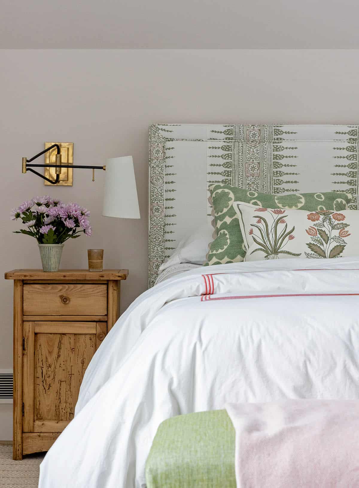 Bedroom with a green block-print upholstered headboard, pine nightstand and brass swing-arm sconce