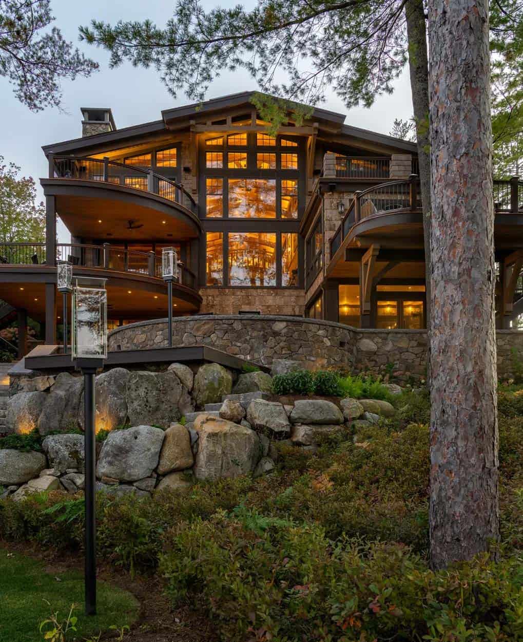 Lakeside facade at twilight with two-story windows, curved decks, and boulder retaining wall