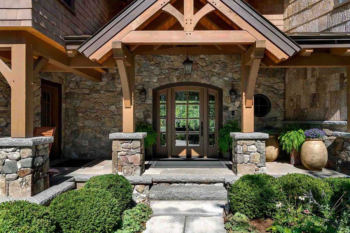 Front entry with timber frame portico, arched wood door, and fieldstone walls
