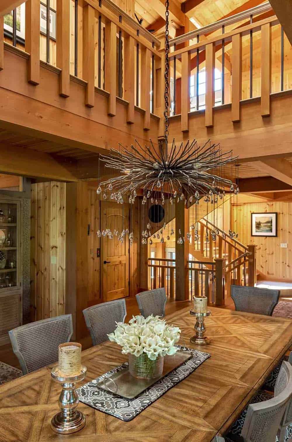Dining room with sculptural crystal chandelier beneath an open timber balcony and staircase