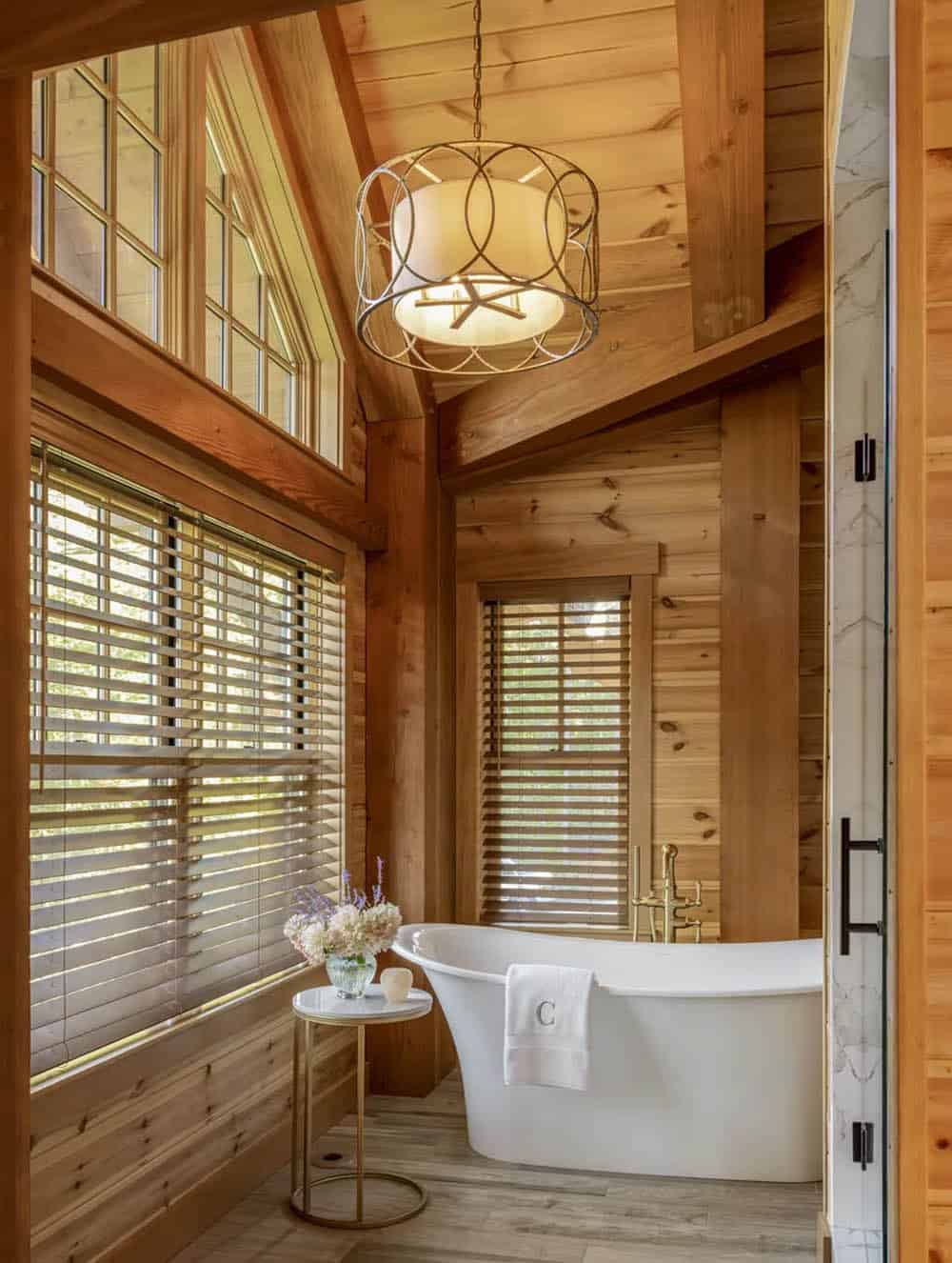 Primary bathroom with freestanding tub, brass tub filler, and drum pendant under a vaulted pine ceiling