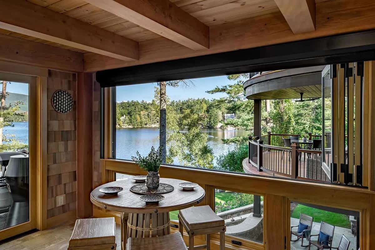 Screen porch with round bistro table and wraparound windows overlooking the lake and curved deck