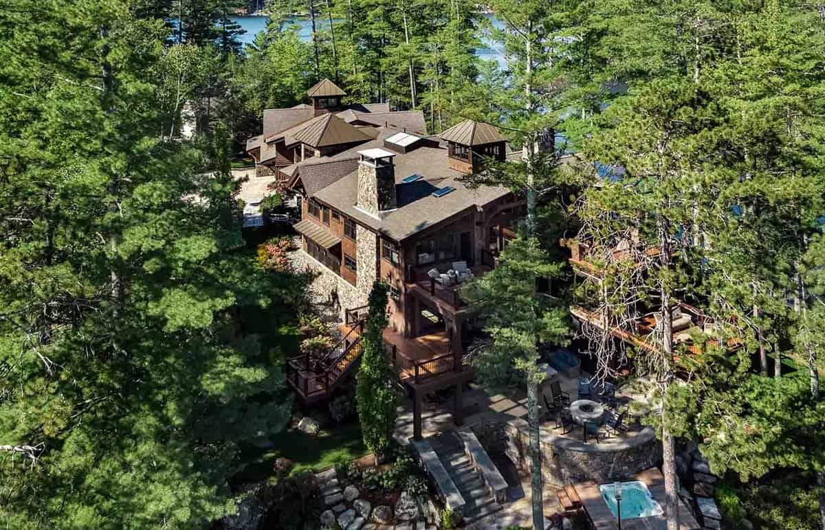 Aerial view of the lodge with stone chimney, cupolas, and fire pit terrace surrounded by pines