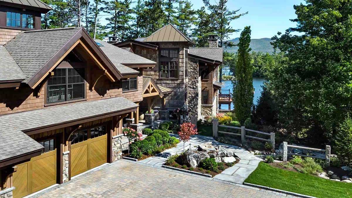 Driveway approach with wood garage doors, fieldstone accents, and a glimpse of the lake