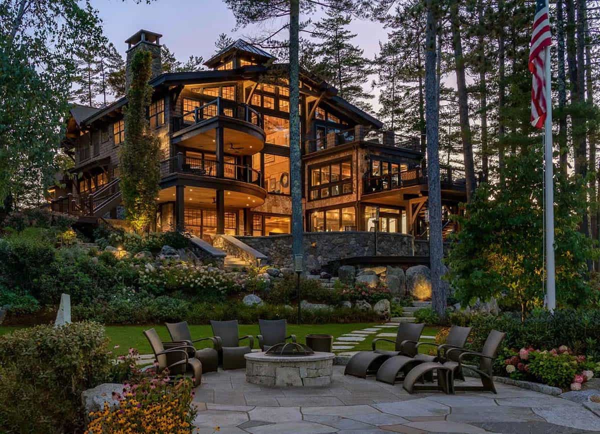 Stone fire pit patio with lounge chairs in front of the illuminated lakeside facade at dusk