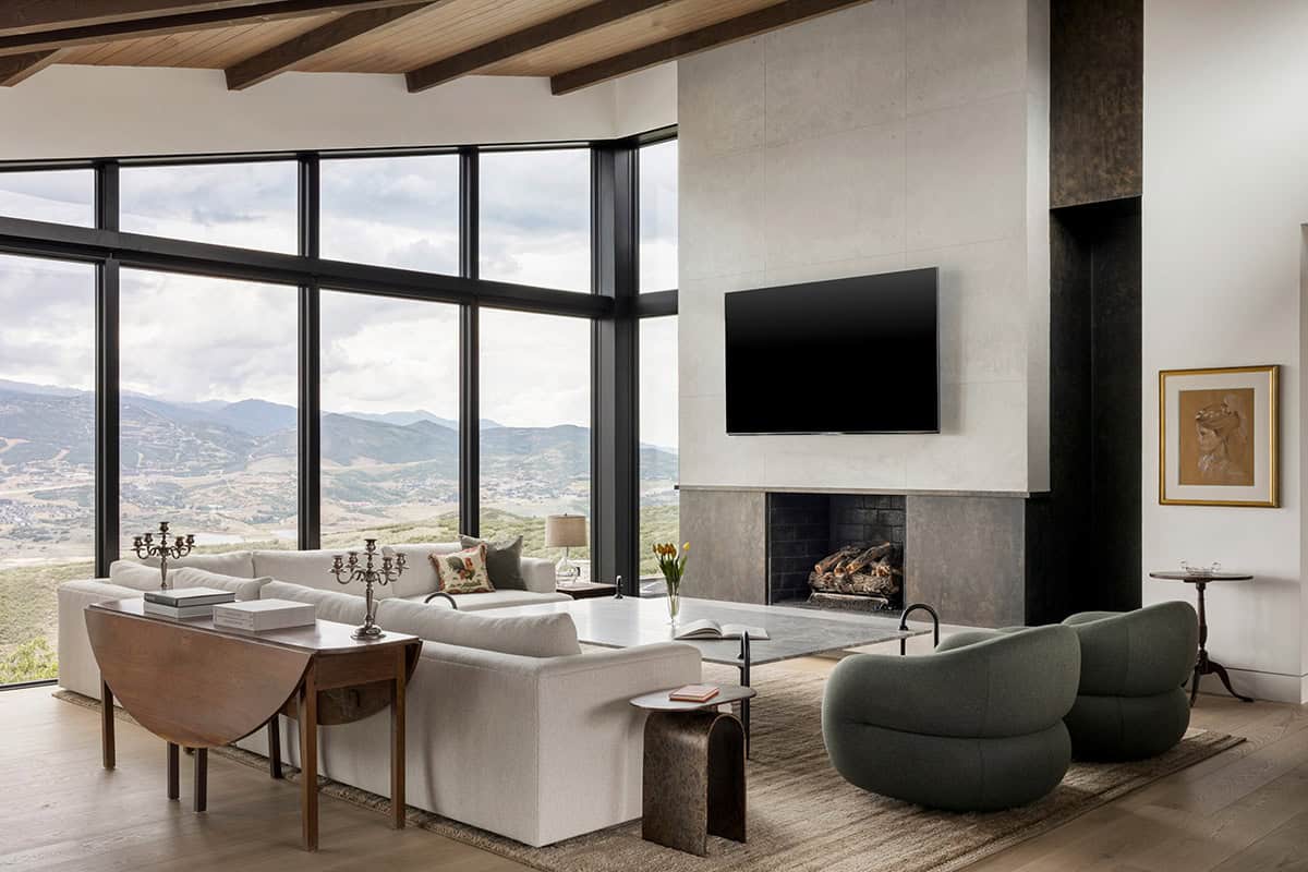 Living room with white sectional, green swivel chairs, and floor-to-ceiling mountain views