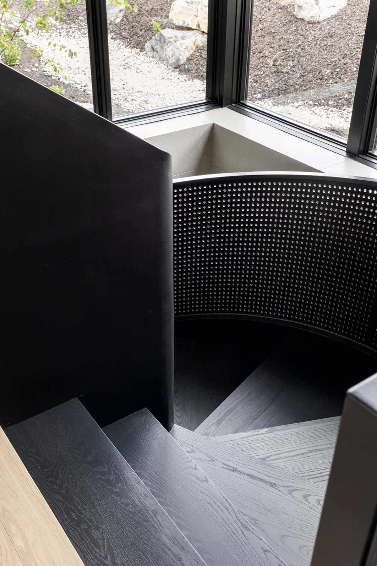 Black oak spiral staircase with perforated steel railing beside corner windows