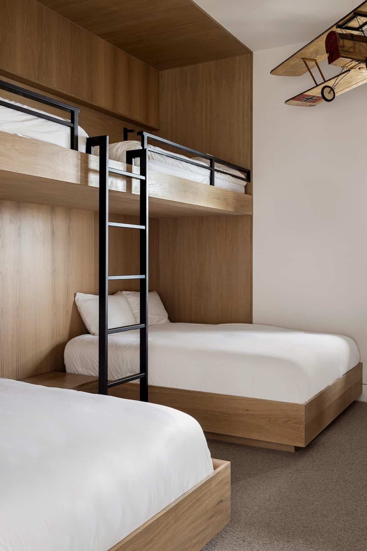 Bunk room with built-in white oak bunk beds, black steel ladder, and model biplane