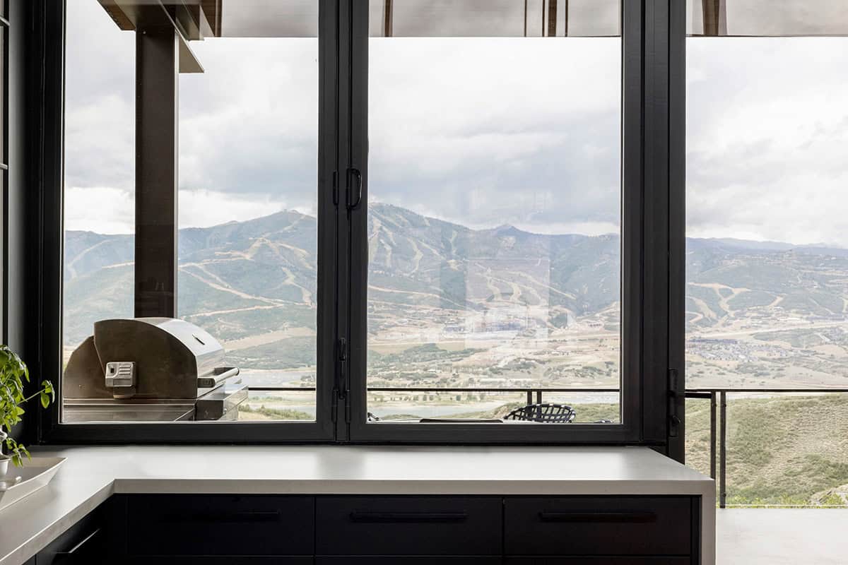 Kitchen counter at bifold window looking out to outdoor grill and mountain view