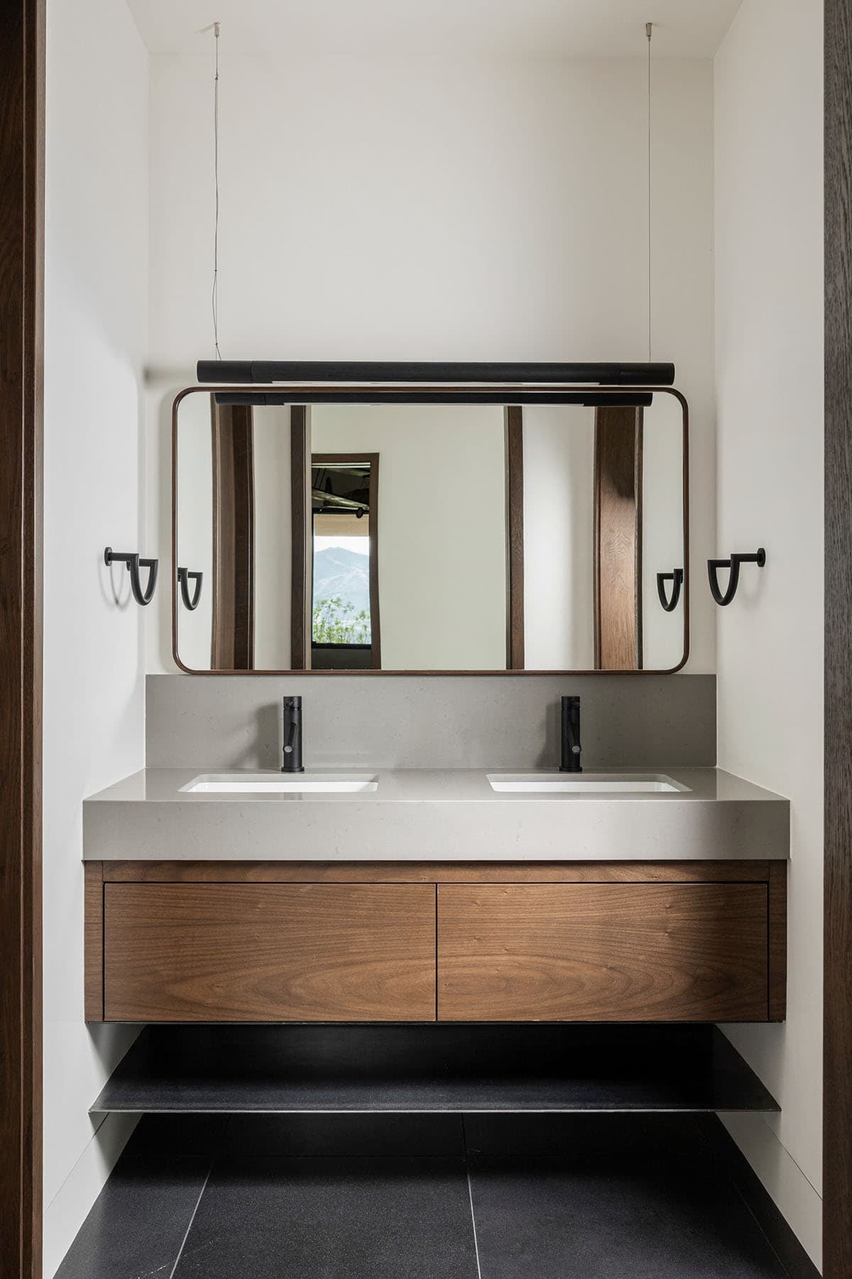 Floating walnut double vanity with gray quartz top and linear pendant light