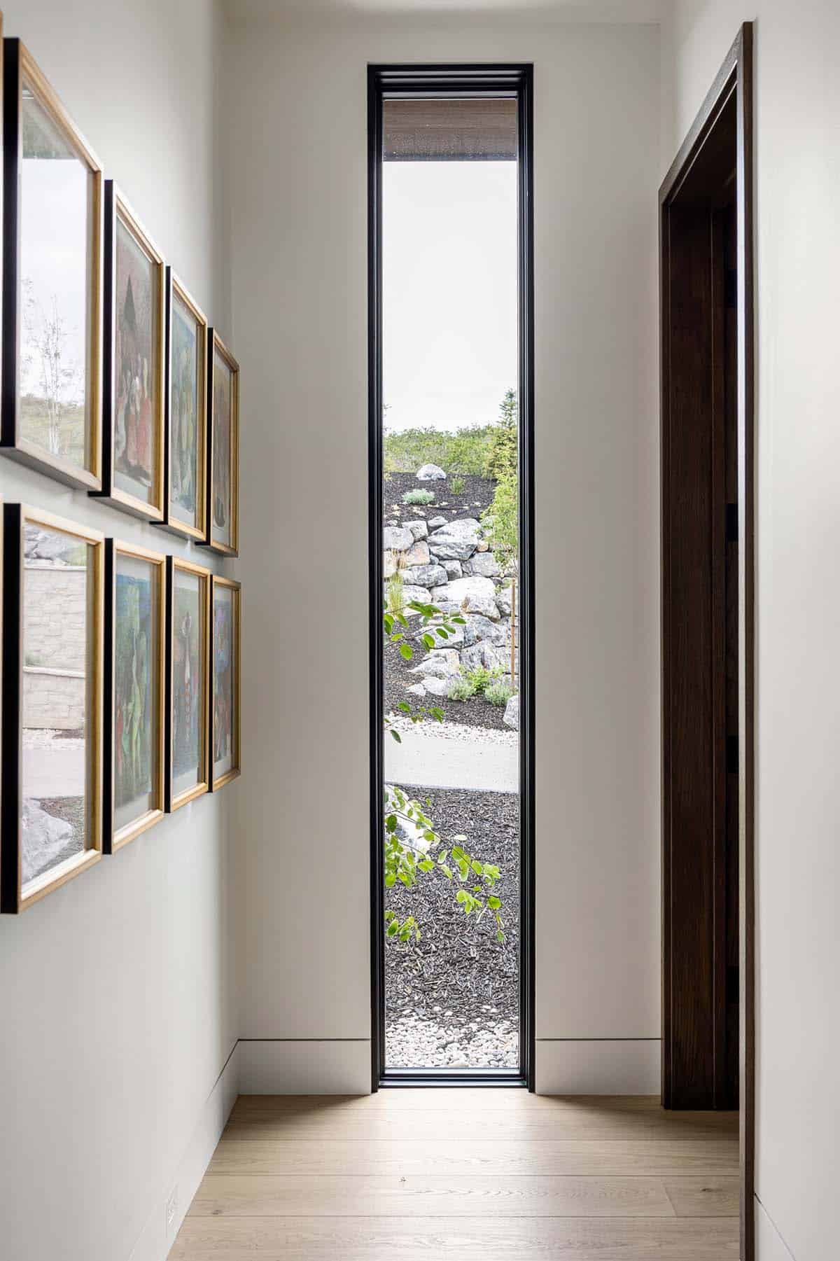 Hallway gallery wall beside tall narrow window framing landscaped hillside