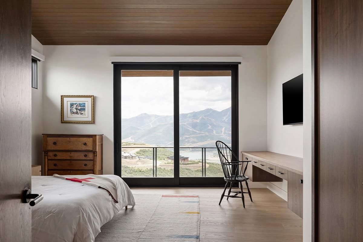 Bedroom with antique dresser, Windsor chair, and sliding doors to mountain view