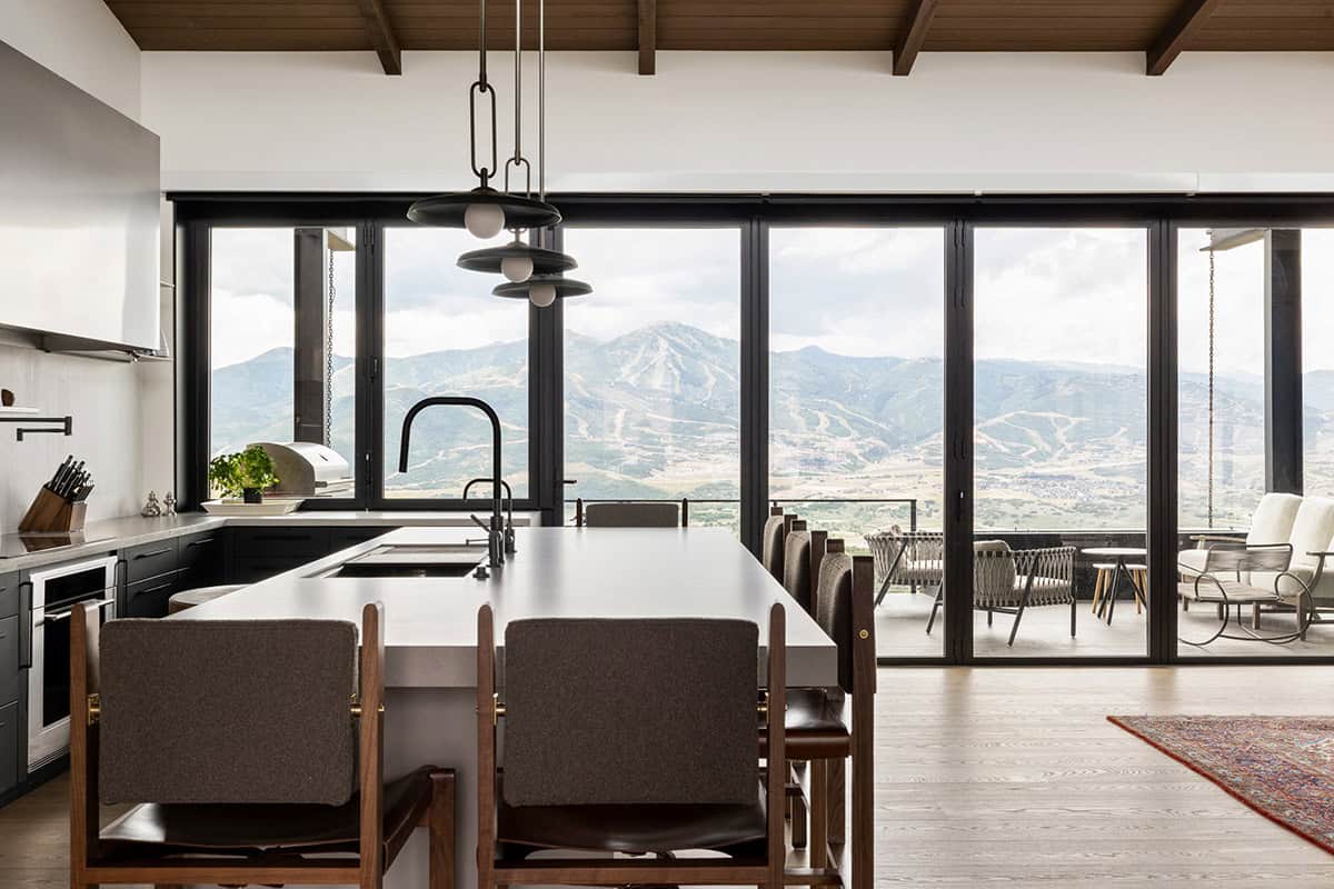 Kitchen island with walnut counter stools facing folding glass wall to terrace