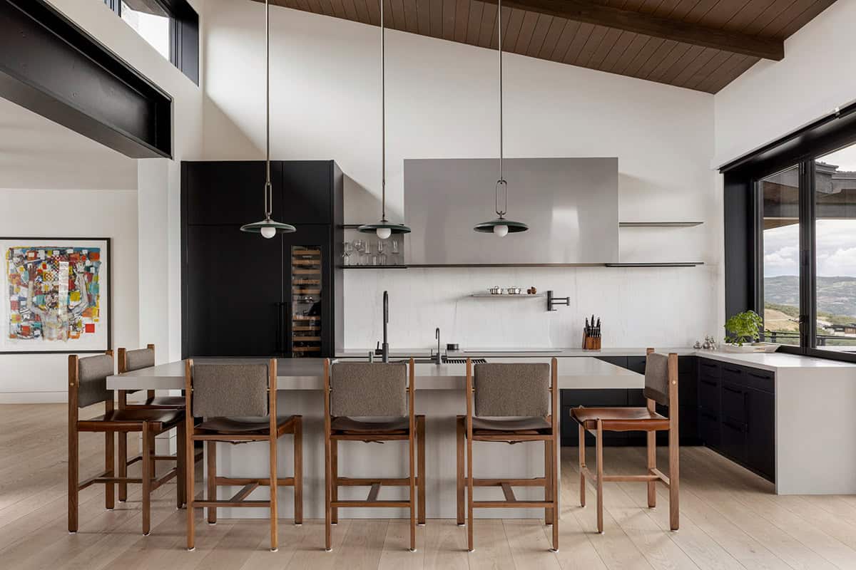 Kitchen with black cabinetry, steel range hood, and three green pendant lights