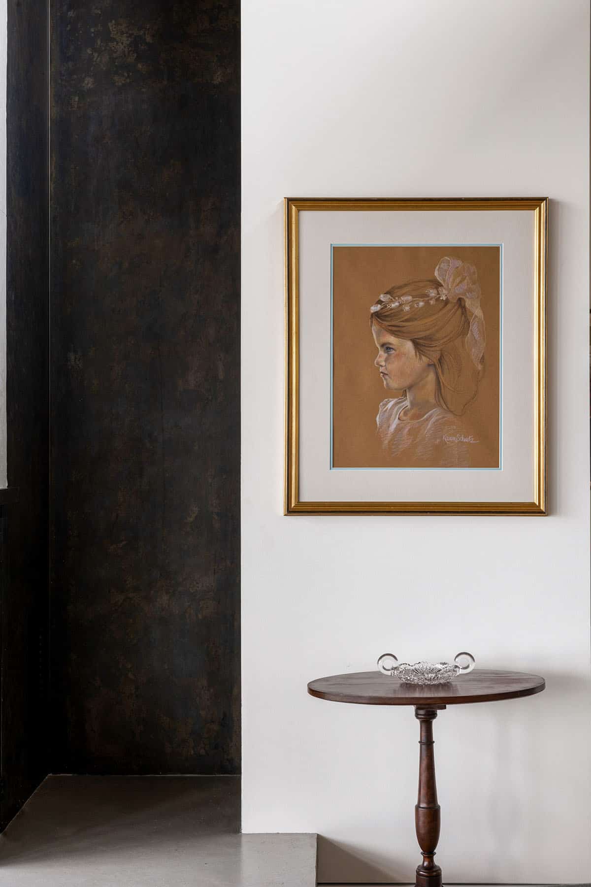 Pastel portrait drawing in gold frame above antique tilt-top table