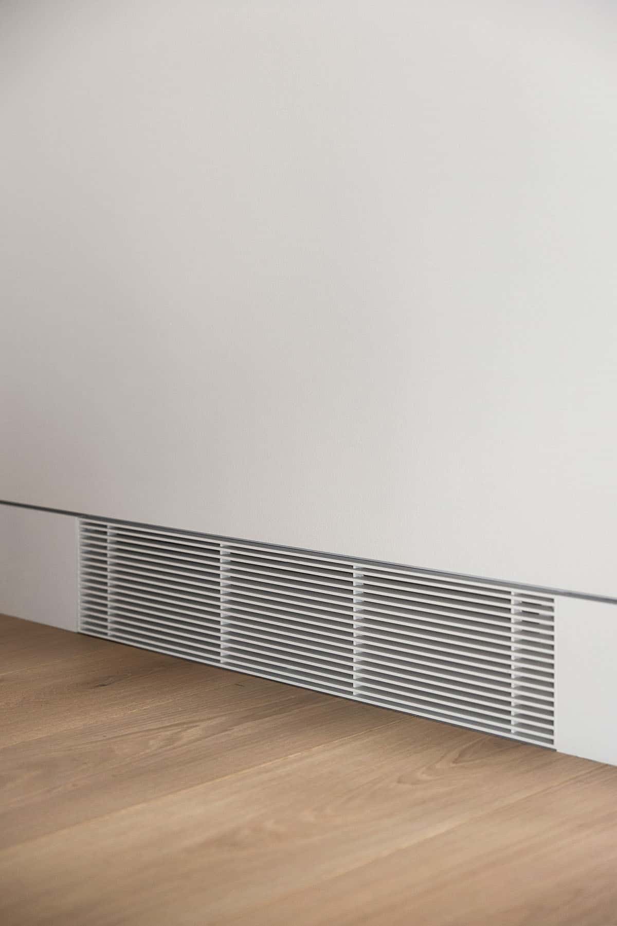 Linear air grille set flush into white wall above oak floor