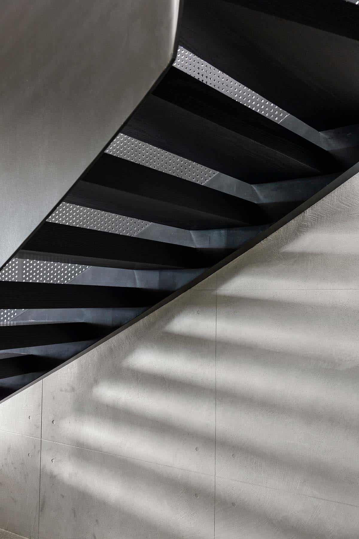 Underside of black oak stair with perforated steel against concrete wall