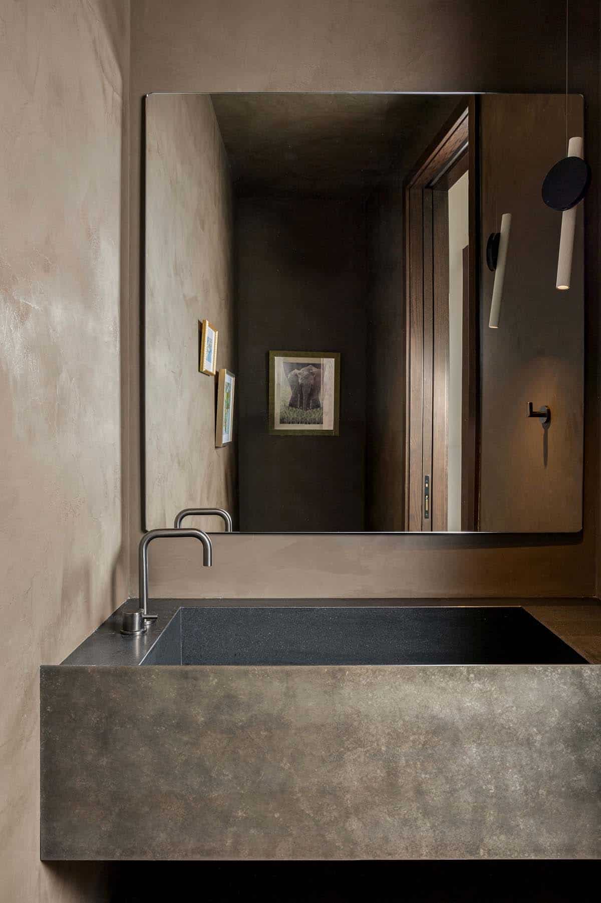 Powder room with earthy plaster walls, stone trough sink, and large mirror