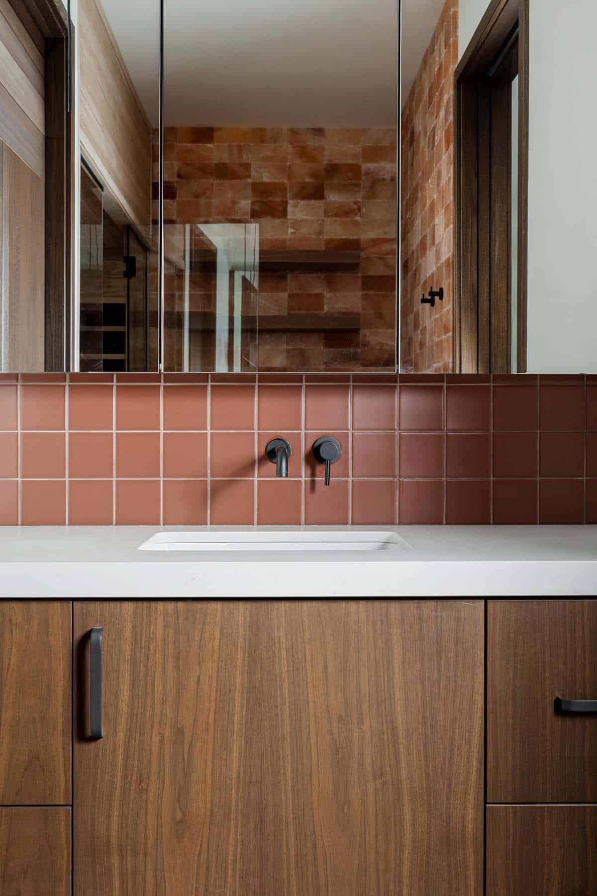 Walnut vanity with terracotta tile backsplash and black wall-mount faucet