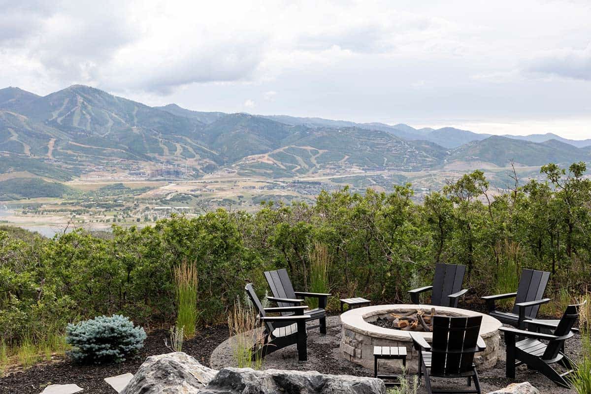 Stone fire pit with black Adirondack chairs overlooking ski mountain and valley