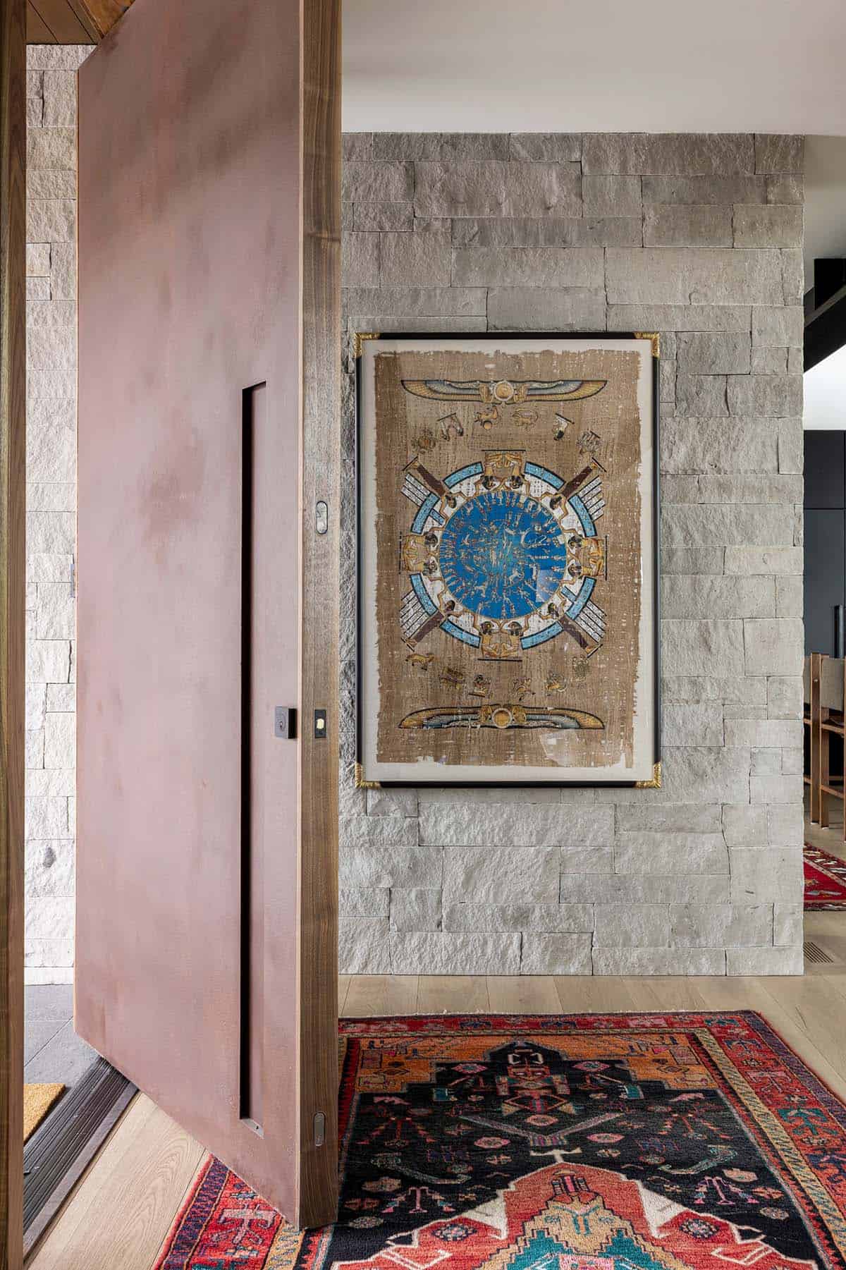 Pivot front door opening to stone wall, framed papyrus, and vintage runner rug