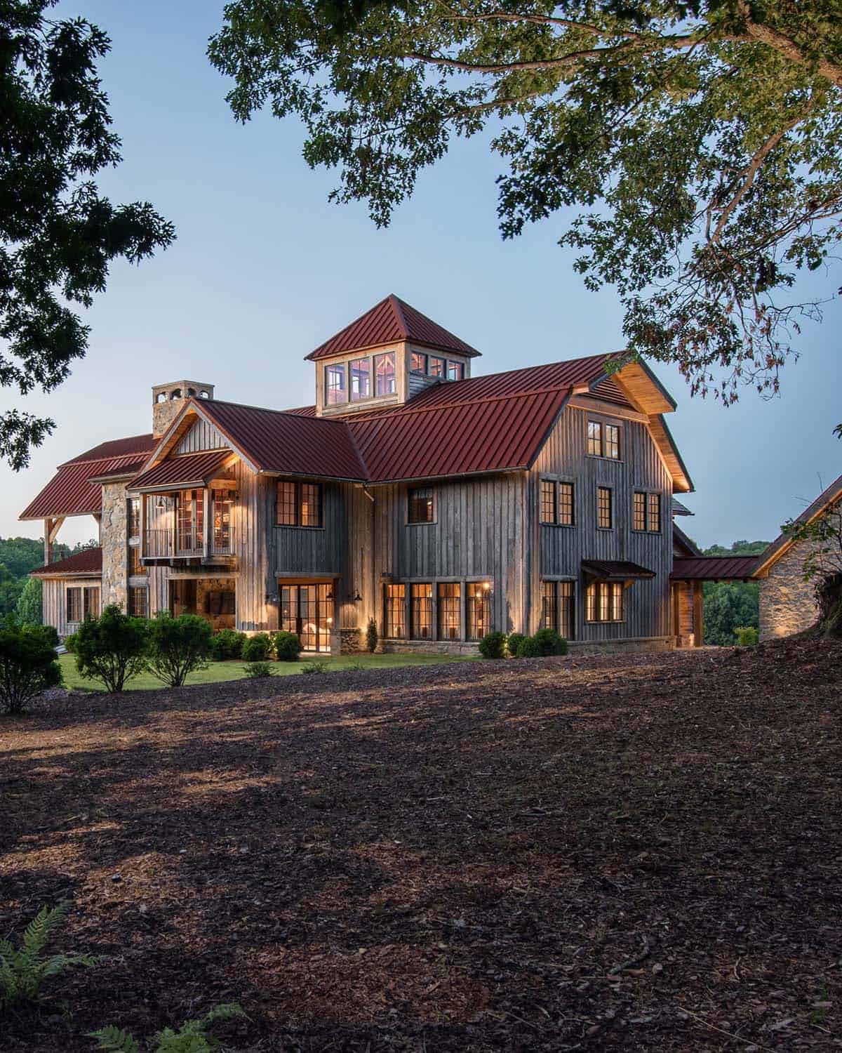 Barn-style home with red metal roof and cupola lit at dusk