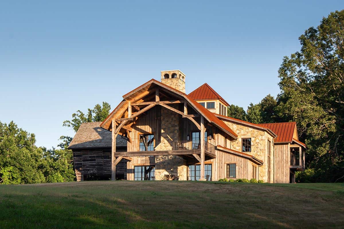 Timber-frame gable porch and stone chimney on a hillside at sunset